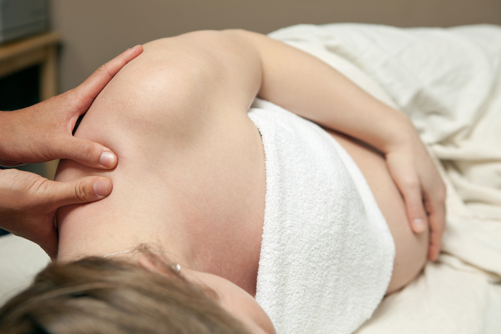 Overhead slanted view of pregnant individual lying on table holding belly while shoulder is massaged