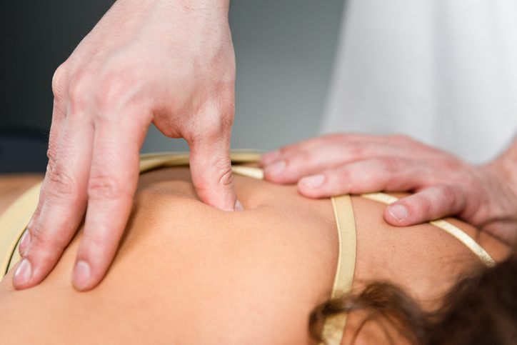 Massage therapist uses fingertips to perform trigger point therapy on client's back and shoulder