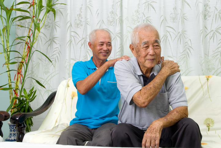 Elderly man holds shoulder while mature adult provides massage in room of house